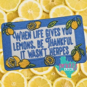 May include: Embroidered patch with a blue border and white center, featuring the text "When life gives you lemons, be thankful it wasn't herpes." Lemon and leaf illustrations adorn the corners. The background is a bed of lemon slices.