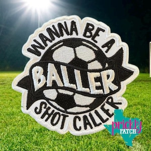 May include: A black and white patch with the text "Wanna Be A Baller Shot Caller" surrounding a soccer ball design. The patch has a white border and is set against a green background. The Prickly Patch logo is in the bottom right corner.