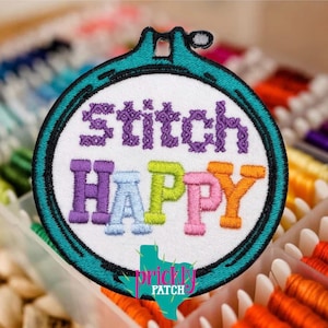 Puede incluir: Parche bordado con las palabras "stitch HAPPY" en morado, azul, verde, rosa y naranja. El parche tiene forma de bastidor de bordado turquesa con fondo blanco. El parche también presenta un logotipo con forma de Texas con las palabras "Prickly Patch".