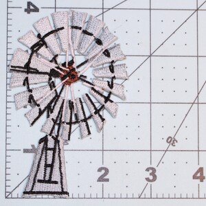 May include: Embroidered windmill patch featuring a detailed design with white blades, black accents, and a brown center. The patch is approximately 3 inches in diameter and is suitable for sewing or ironing onto fabric items. Ideal for adding a rustic touch to clothing or accessories.