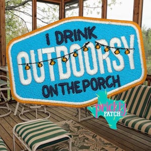 May include: A blue embroidered patch with an orange border featuring the text I DRINK OUTDOORSY ON THE PORCH in white and dark blue. A string of small yellow string lights is stitched across the center of the patch above the word OUTDOORSY.