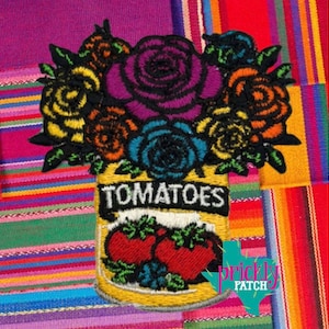 May include: Embroidered patch featuring a bouquet of colorful roses in a yellow jar labeled "TOMATOES." The roses are in shades of purple, blue, orange, and yellow with black outlines. The jar has two red tomatoes and the text "TOMATOES".