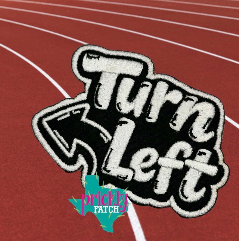 K&ouml;nnte beinhalten: Gestickter Aufn&auml;her mit den Worten "Turn Left" in Wei&szlig;, schwarz umrandet, mit einem nach links zeigenden Pfeil. Der Aufn&auml;her hat einen schwarzen Hintergrund und einen wei&szlig;en Rand. Der Aufn&auml;her befindet sich auf einer roten Laufstrecke.