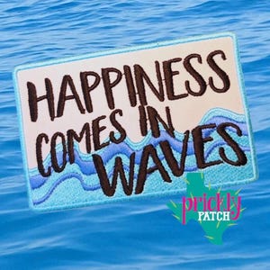 May include: A rectangular patch with the words "HAPPINESS COMES IN WAVES" embroidered in brown thread. The design includes blue waves and a light beige background, set against a blue water backdrop. The patch has a turquoise border and a logo in the bottom right corner.