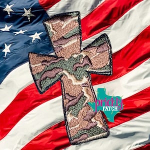 May include: Embroidered cross patch with a camouflage pattern, set against the backdrop of the American flag. The cross features shades of brown, green, and purple. The image includes the text "prickly patch".