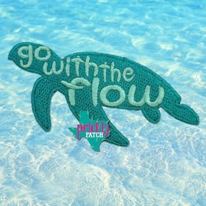 May include: A teal embroidered patch shaped like a sea turtle with the text go with the flow stitched in a lighter shade of teal across the body. A small teal star-shaped logo with the text prickly patch is positioned over the lower fin.