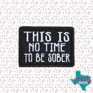 May include: Black rectangular patch with white embroidered text that reads "THIS IS NO TIME TO BE SOBER." The patch is set against a white background with a repeating pattern of pink and green lines. A teal Texas-shaped logo is in the bottom right corner.