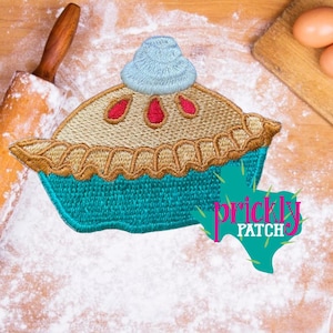 May include: Embroidered patch in the shape of a pie with a blue crust and whipped cream topping. The pie has a tan crust and filling with red berry accents. The patch has the text "prickly patch" in pink and green.
