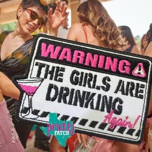May include: Embroidered patch with the text "WARNING THE GIRLS ARE DRINKING Again!" in black and pink. The patch features a cocktail glass and a Texas-shaped logo. The background shows a party scene with people dancing.
