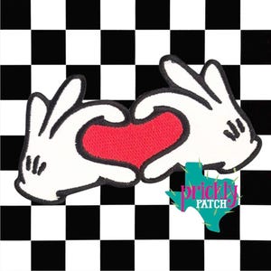 May include: Embroidered patch featuring white cartoon hands forming a red heart shape. The patch has a black outline and is set against a black and white checkered background. The patch includes the text "prickly patch" in a turquoise Texas-shaped logo.