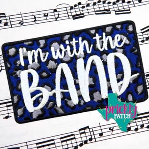 May include: A rectangular embroidered patch featuring a blue and grey leopard print background with the white stitched text I'm with the BAND. The patch has a thick black border and is displayed against a background of printed musical notes.
