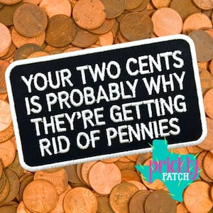 May include: A rectangular black embroidered patch with white stitched text that reads: YOUR TWO CENTS IS PROBABLY WHY THEY'RE GETTING RID OF PENNIES. The patch features a white border and is placed against a background of numerous copper pennies.