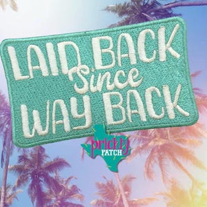May include: A rectangular embroidered patch with a teal background and white stitched text that reads LAID BACK Since WAY BACK. Below the patch is a small teal Texas-shaped logo with the pink and white text Prickly PATCH.