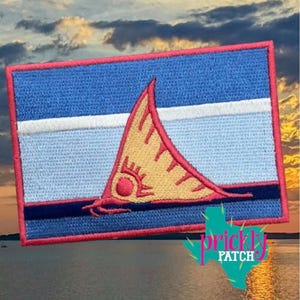May include: Embroidered patch featuring a rectangular design with a blue background, a white stripe, and a yellow sail-like shape. The patch has a red border and a navy blue stripe. The patch is labeled "prickly patch".
