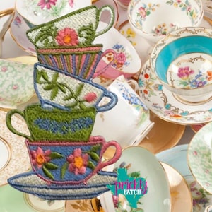 May include: An assortment of embroidered teacups and saucers in various colors and floral designs. The teacups are stacked, showcasing detailed stitching and vibrant hues. Other teacups and saucers with floral patterns are scattered around.