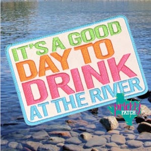 May include: Embroidered patch with the text "IT'S A GOOD DAY TO DRINK AT THE RIVER" in green, orange, pink, and blue. The patch has a white background and a blue border. A green and turquoise cactus logo is in the lower right corner.