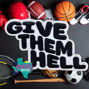 May include: A white embroidered patch with thick black lettering that reads GIVE THEM HELL. The patch is surrounded by various sports equipment including a red helmet, a football, a basketball, a baseball bat, a football, and a tennis racket.