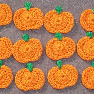 May include: A collection of twelve crocheted pumpkins. Each pumpkin is orange with a green stem. The pumpkins are arranged in three rows of four, perfect for fall-themed crafts and decorations.