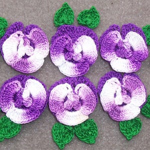 May include: Six crocheted purple and white pansies with green leaves. The pansies are ombre, fading from purple to white.