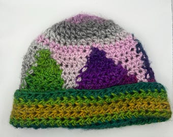 May include: A handmade crochet beanie in a variety of colors. The hat features a green, yellow, and dark green brim. The crown of the hat has a pattern of green, purple, pink, and gray sections.