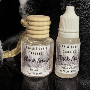 May include: Two small glass bottles of Lena & Lonnie Candles Black Snow scented car diffuser and diffuser refill. The diffuser bottle has a wooden top and a label with the product name and scent. The refill bottle has a white cap and a label with the same information. Both bottles are 0.27 OZ (8ML).