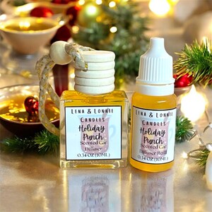 May include: Two car air fresheners with the text "Lena & Lonnie Candles Holiday Punch". One is a square diffuser with a wooden top and a braided rope. The other is a refill bottle. Both contain 0.34 oz (10ml) of liquid.
