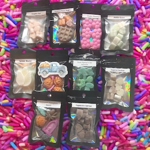 May include: Assortment of scented wax melts in various shapes and colors, packaged in black resealable bags. The bags are labeled with names like "Pumpkin Chai," "Violet Flannel," and "Caramel Pumpkin Swirl." The background is a colorful mix of sprinkles.