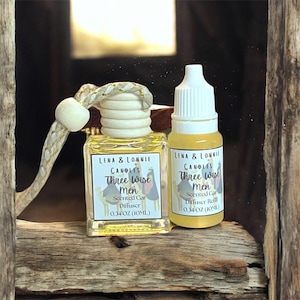 May include: A car air freshener and refill set. The car diffuser is a small, square glass bottle with a wooden top and a decorative cord. The refill bottle is cylindrical. Both bottles have labels that read "Three Wise Men".