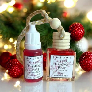 May include: Two car air fresheners with "Christmas Berry" scent. One is a refill bottle, the other a diffuser. Both have labels with the brand name "Lena & Lonnie Candles". The refill bottle contains a red liquid. The diffuser is a small, square glass bottle.