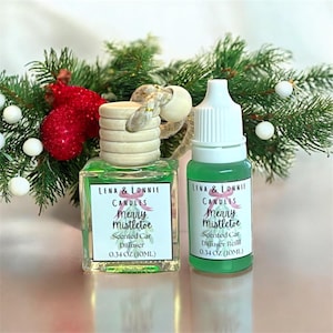 May include: A green car air freshener and refill bottle with the text "Merry Mistletoe" and "Lena & Lonnie Candles". The bottles are 0.34 oz (10ml) and are in front of a Christmas decoration.