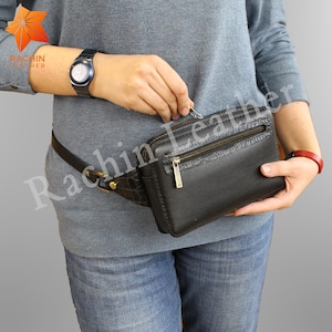 Könnte beinhalten: Eine schwarze Leder-Bauchtasche mit einem krokodilgeprägten Design. Die Tasche hat einen Reißverschluss und einen Schnallenriemen.