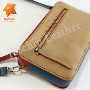 May include: A tan leather wallet with a blue and red trim. The wallet has a gold zipper and a strap. The brand name "Rachin Leather" is printed on the front of the wallet.