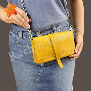May include: A mustard yellow leather crossbody bag with a textured finish. The bag has a flap closure with a strap and a chain strap. The brand name "Rachin Leather" is visible on the bag.