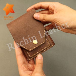May include: A brown leather wallet with a flap and a snap closure. The wallet has a stitched border and a gold-colored snap. The logo "Rachin Leather" is visible in the upper left corner.