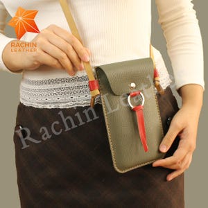 Könnte beinhalten: Olivgrüne Leder-Umhängetasche für Telefone mit Klappe und rotem Akzent. Die Tasche hat einen beigefarbenen Riemen und ein rotes Leder-Loop-Detail. Der Markenname "Rachin Leather" ist sichtbar.