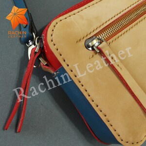 May include: A close-up of a small, tan leather wallet with a blue and red trim. The wallet has a zipper closure and a gold zipper pull. The brand name "Rachin Leather" is printed on the wallet.