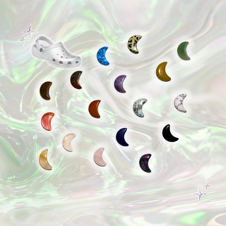 May include: A white Croc shoe is positioned near a collection of crescent-shaped charms in various colors and textures. The charms include shades of blue, brown, pink, and green, with speckled and marbled patterns. The background has a pearlescent, iridescent effect.