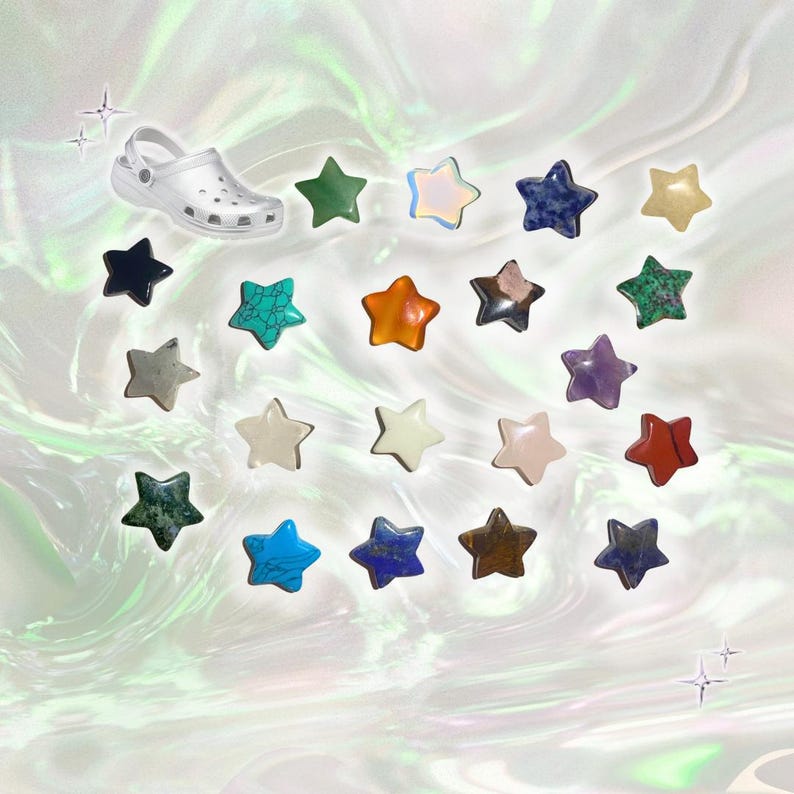 May include: A collection of star-shaped charms in various colors and materials, including green, blue, and orange, alongside a white clog shoe. The charms appear to be made of gemstones and other materials. The background has a pearlescent, iridescent effect.