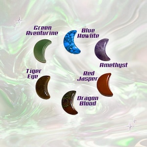 May include: A collection of crescent-shaped gemstones, including Green Aventurine, Blue Howlite, Amethyst, Tiger Eye, Red Jasper, and Dragon Blood. Each stone is labeled with its name in a stylized font, set against a swirling, iridescent background.