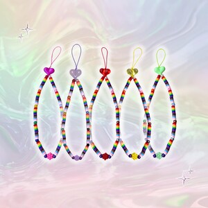 Puede incluir: Cinco colgantes de teléfono con cuentas de colores del arcoíris. Cada colgante tiene una cuenta en forma de corazón en la parte superior, en rosa, transparente, rojo, amarillo y verde. Los colgantes están ensartados con cuentas coloridas y tienen un lazo en la parte superior.
