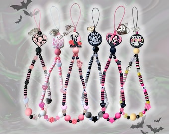 May include: Six beaded phone charms featuring various charms including skulls, ghosts, and horror-themed icons. Each strap is composed of black, pink, and white beads in assorted shapes, including hearts and stars, with attached loops for attachment.