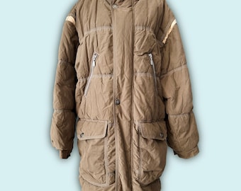 May include: A long, brown puffer coat with a high collar and multiple pockets. The coat features a quilted design, a zipper closure, and button details. The sleeves have a slight puff, and there are light-colored stripes on the shoulders.