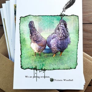 Könnte beinhalten: Ein Stapel Grußkarten mit einer Aquarellillustration von zwei Hühnern auf grünem Gras. Das Bild enthält den Text "We are plotting revolution." und den Namen "Victoria Woodhull."