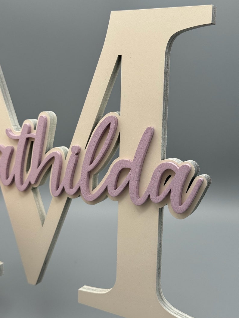 May include: A white wooden letter M with the name "Mathilda" written in pink on it.