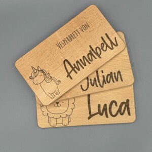 May include: Three wooden snack boards with engraved names and animal illustrations. The top board says "Vesperbrett von Annabell" with a unicorn illustration. The middle board says "Julian" and the bottom board says "Luca" with a lion illustration.