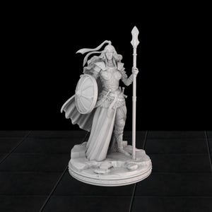 以下が含まれることがあります： 槍と盾を持った、鎧を着た女性戦士の精巧な白い置物。フィギュアは、円形の縁が付いた岩の台座の上に立っています。戦士は長い髪をしており、ヘルメット、鎧、そして流れるようなケープを身に着けています。