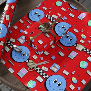 May include: Red wrapping paper with a repeating pattern of blue smiley faces, floppy disks, and cassette tapes. The paper is wrapped around a small gift box with a brown ribbon.