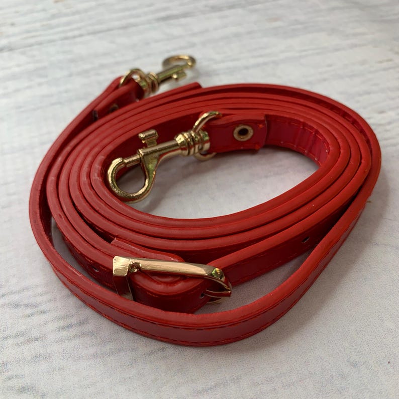 Puede incluir: Una correa de bolso roja brillante enrollada con cierres y herrajes de metal dorado. La correa est&aacute; hecha de un material liso, posiblemente similar al cuero. Los cierres est&aacute;n dise&ntilde;ados para sujetarse a un bolso.