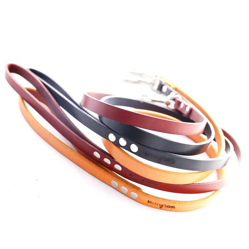 May include: Four leather dog leads in different colours, including orange, brown, red, and black. Each lead has silver metal accents and the brand name "mimigreen" is embossed on the leads.