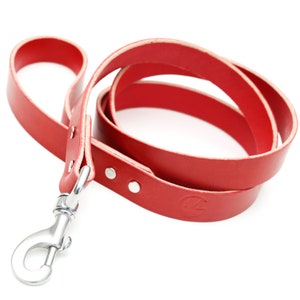 May include: A red leather dog lead with a silver clip. The lead is coiled and has a small logo embossed on the leather.